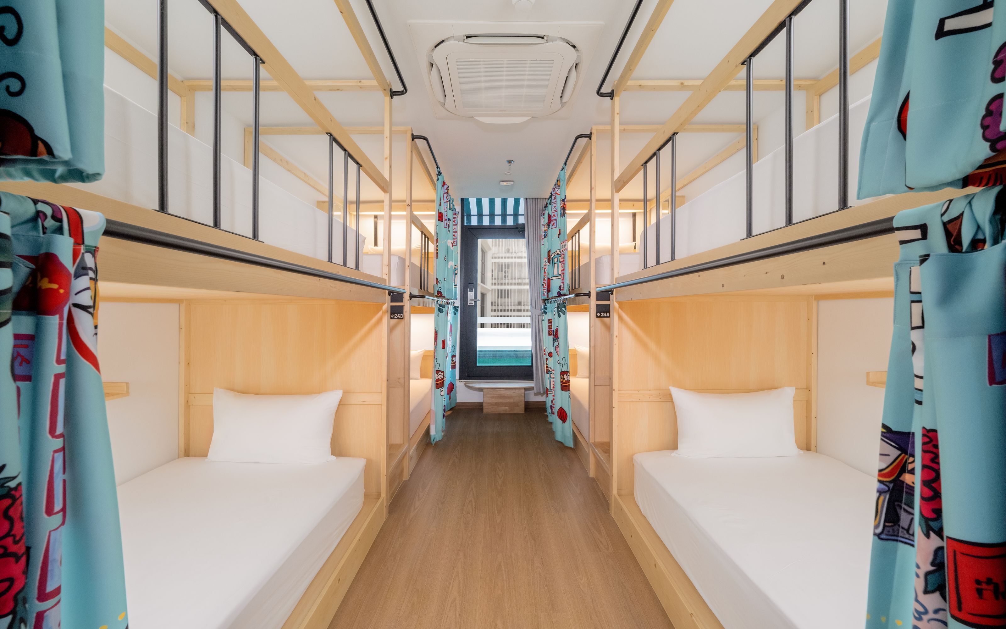 A narrow corridor with bunk beds on either side, a central door leading to a balcony, and a ceiling fan.