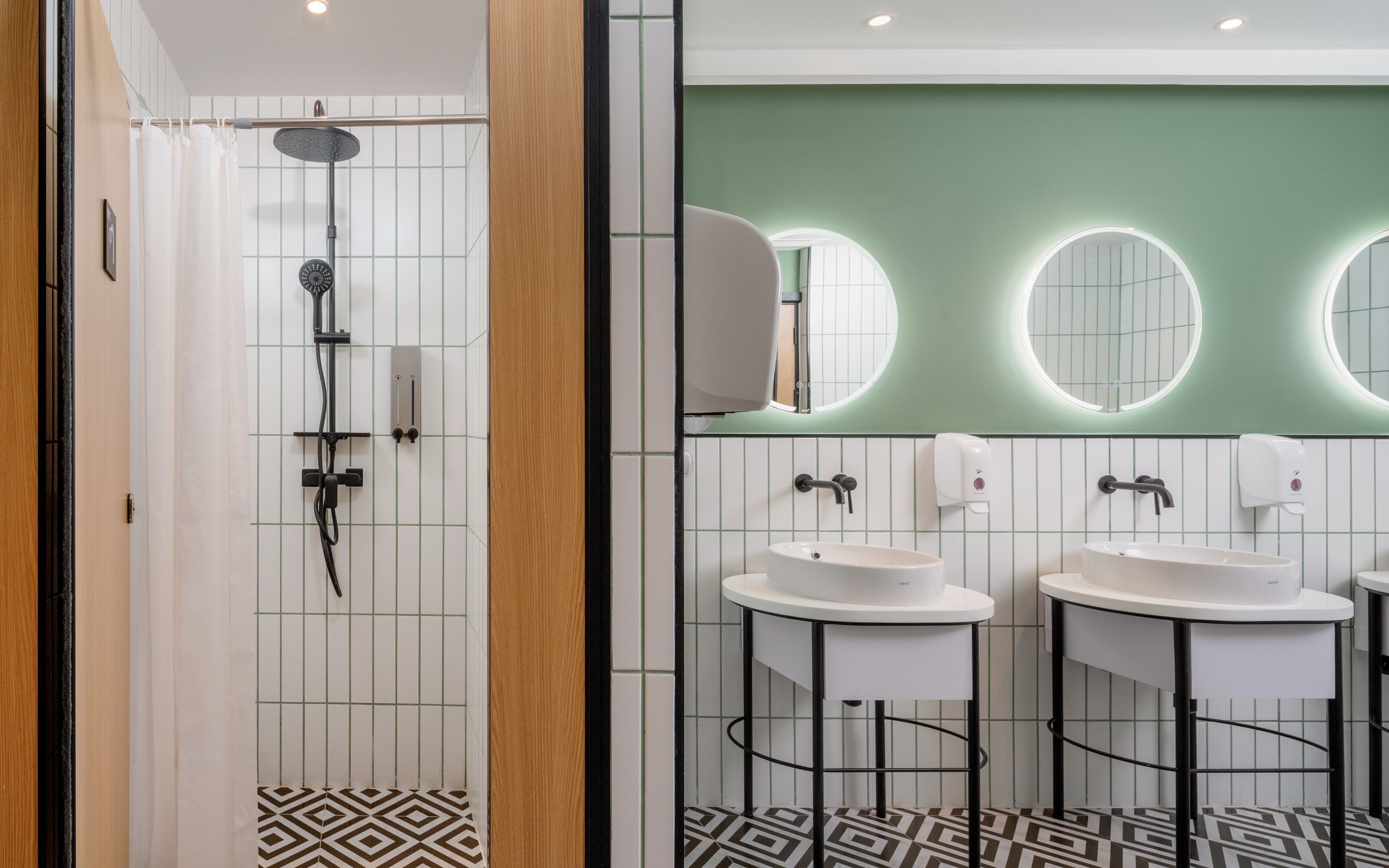 A modern bathroom with a shower, two sinks, and a mirror with circular lights.