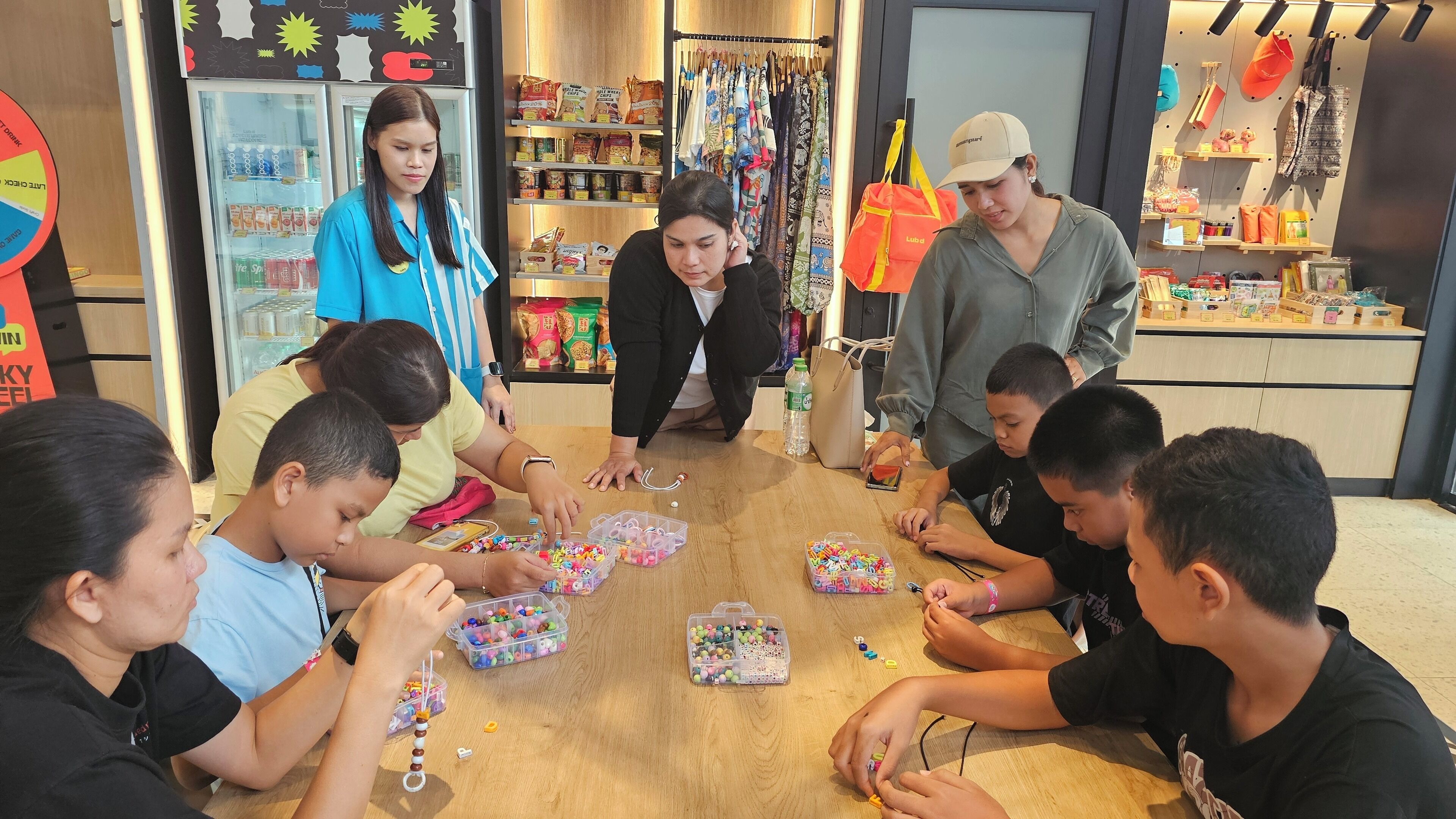 A group of children engaged in a craft activity with beads and strings, surrounded by various items and a store setting.