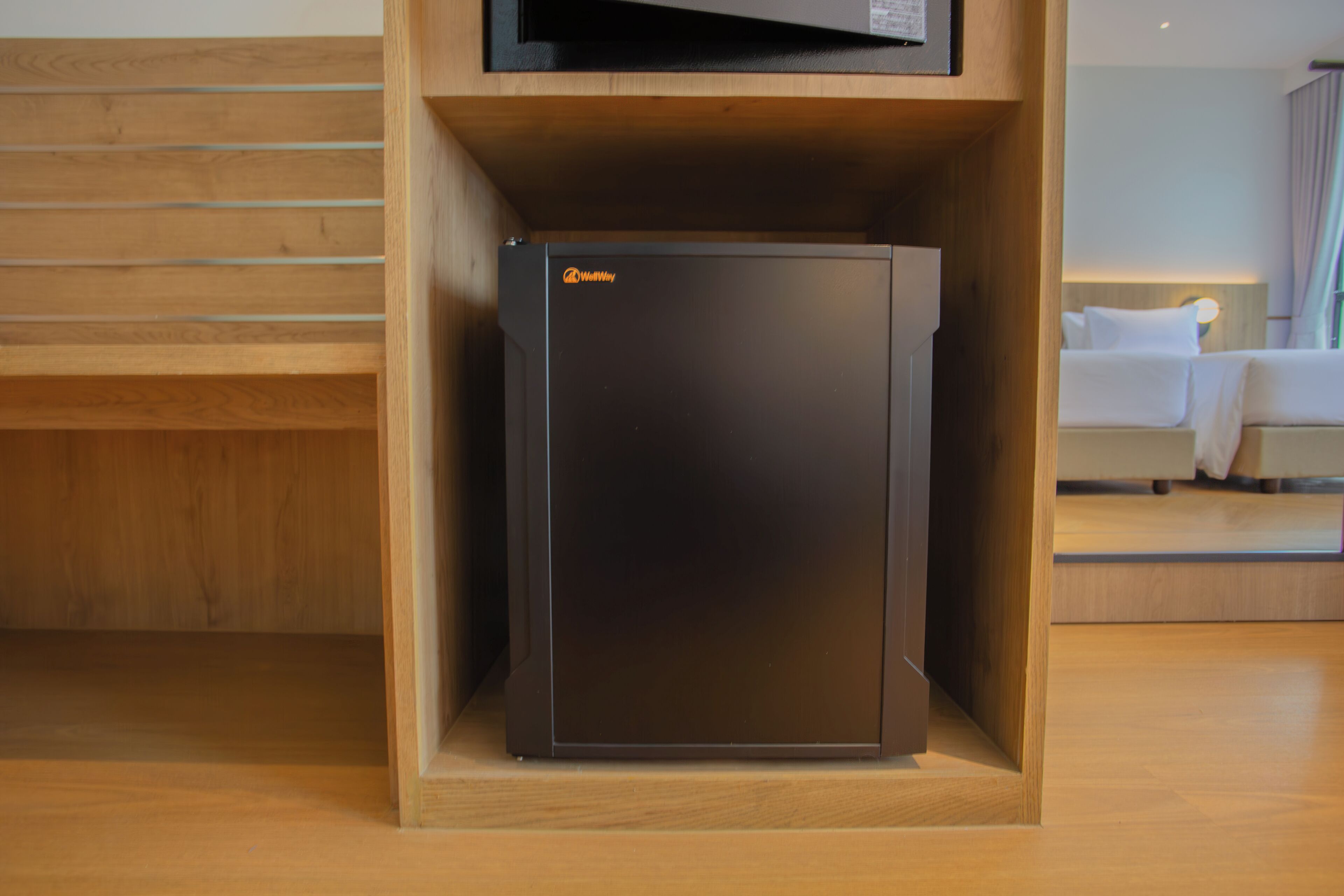 A compact, dark-colored refrigerator in a wooden cabinet, likely in a hotel room.