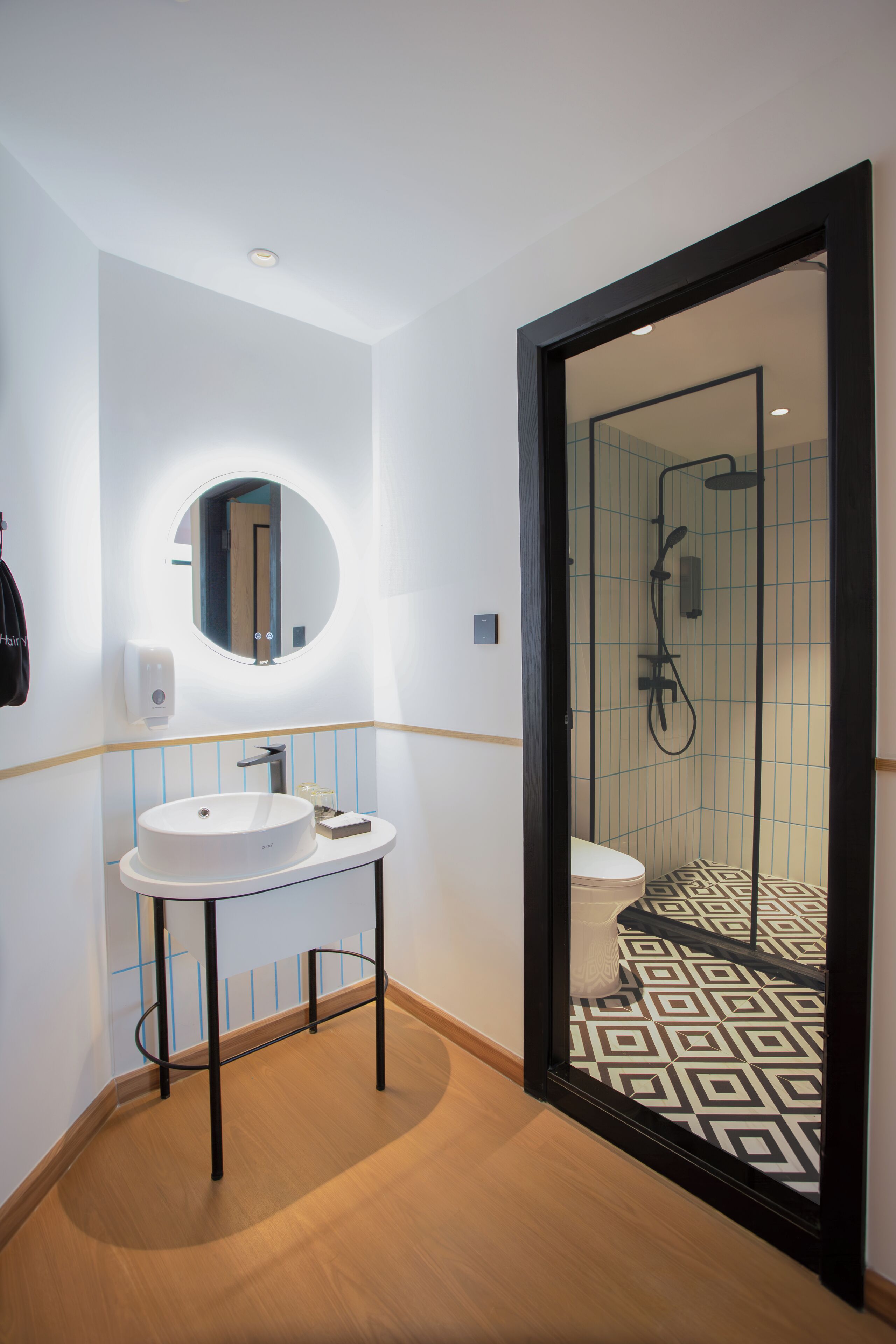 A modern bathroom with a round mirror, white sink, and black-framed shower enclosure.