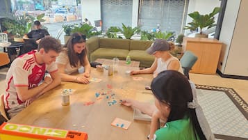 Eine Gruppe spielt UNO an einem Holztisch in einem Raum mit Topfpflanzen und einem grünen Sofa.