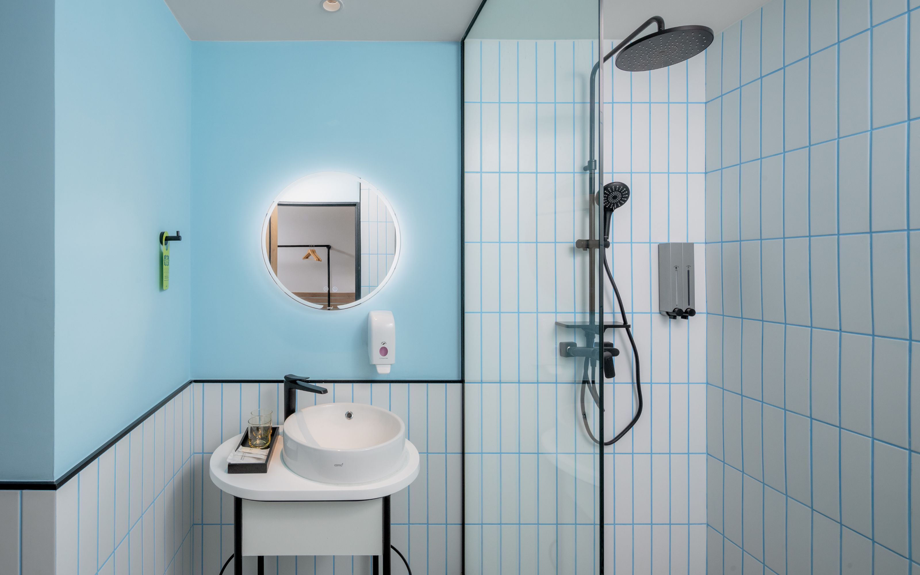 Un baño con un espejo redondo, un lavabo blanco y una ducha con cabezal de ducha de mano.