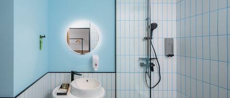 A bathroom with a round mirror, a white sink, and a shower with a handheld showerhead.