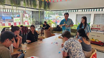 Un grupo de personas jugando un juego de mesa en una habitación con una gran mesa, sillas y una máquina expendedora que dice "Lud d Muse".