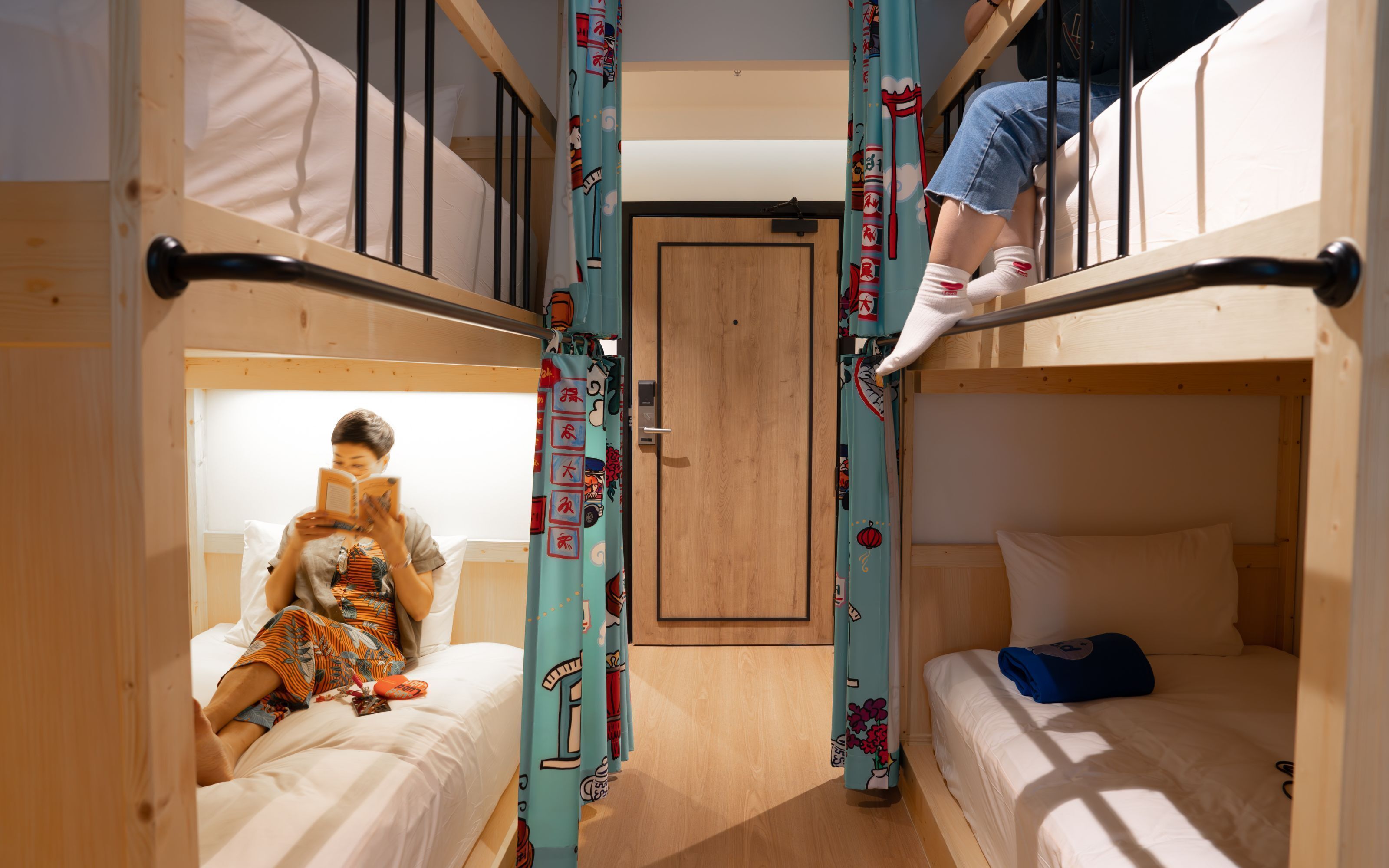 A dormitory room with bunk beds, a door, and a person reading a book.
