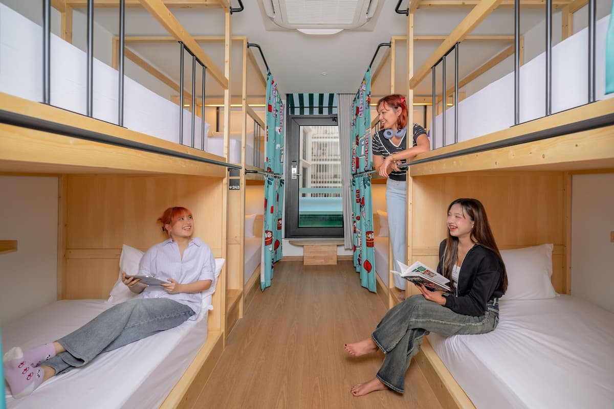 Une chambre de dortoir avec des lits superposés, un couloir central et une fenêtre avec des rideaux.