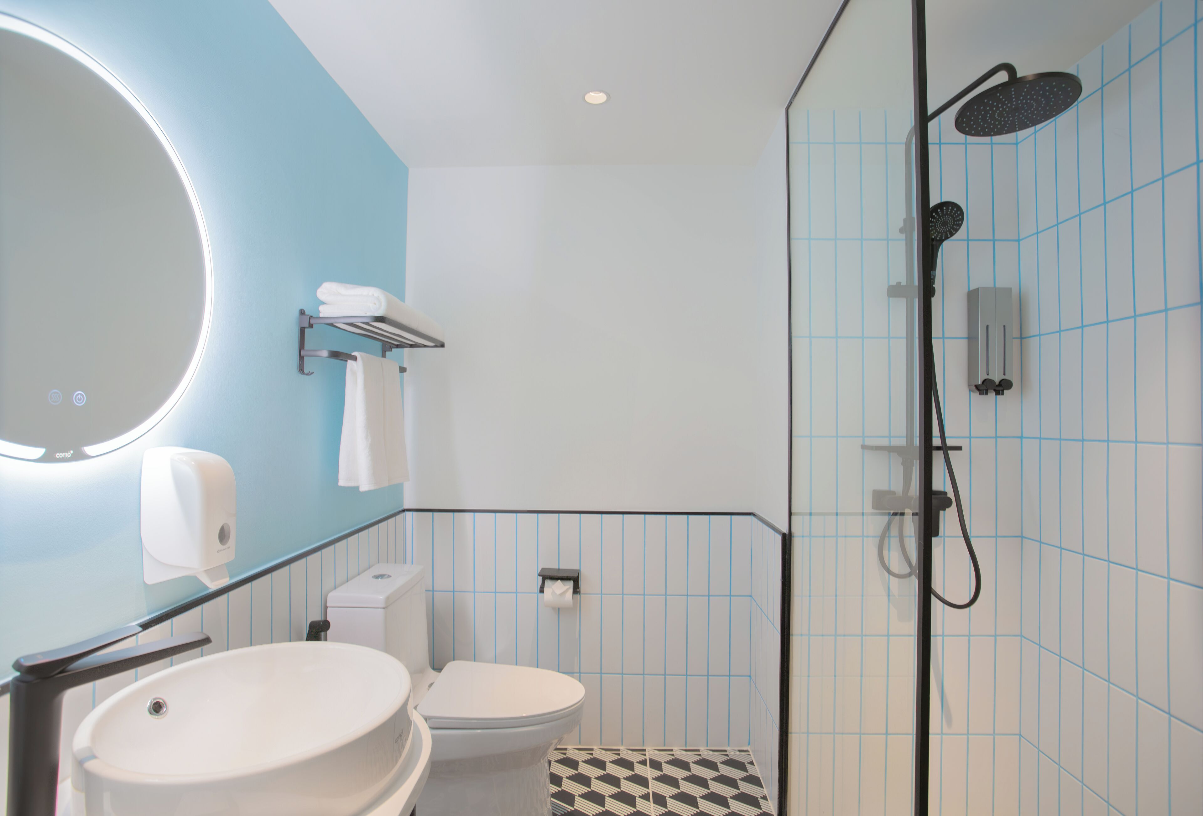 A modern bathroom with a round mirror, a sink, a toilet, and a shower with a handheld showerhead.