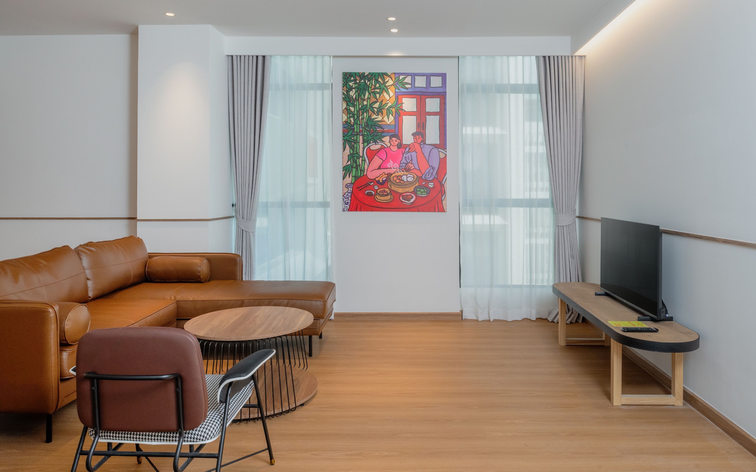 Un salon moderne avec un canapé en cuir, une table ronde en bois, une chaise noire et blanche, un téléviseur à écran plat et un tableau coloré accroché au mur.