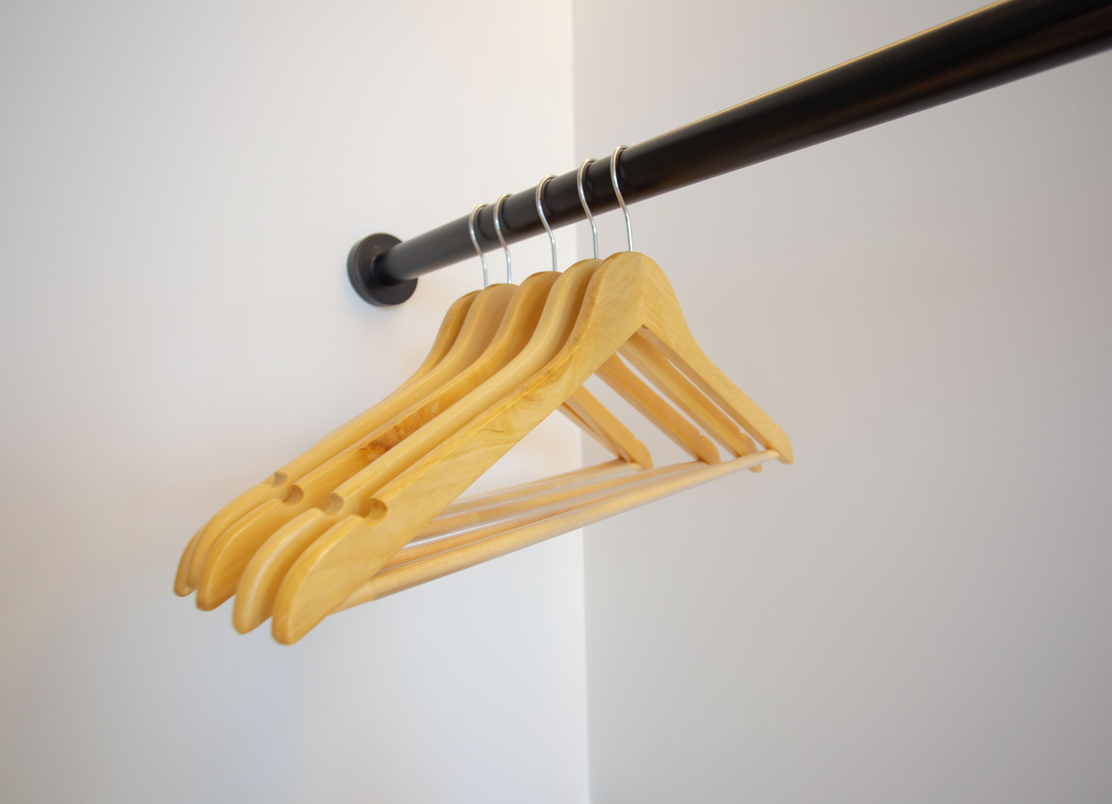 A wooden coat rack with multiple hangers against a white wall.