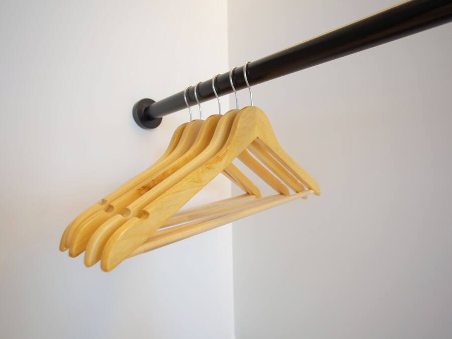 A wooden coat rack with multiple hangers against a white wall.