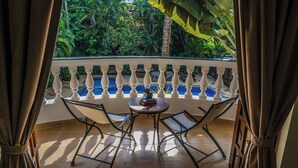 A balcony with a white balustrade, a round table with two chairs, and a view of a pool and lush greenery. - Olive Hotel Alidia Beach Resort by Embassy Group (Baga)