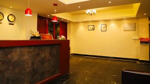 A hotel reception area with a red reception desk, two wall clocks, a chandelier, and framed artwork on the walls. - The Mansarovar Hotel & Banquet (Gangtok)