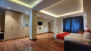 A modern hotel room with a bed, a sofa, a glass coffee table, a wardrobe, and a TV on the wall. - The Mansarovar Hotel & Banquet (Gangtok)