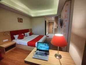 Une chambre d’hôtel avec un lit, un bureau avec un ordinateur portable, une table de chevet et une lampe rouge.