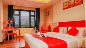 A hotel room with a large bed, a desk with a chair, a window with a mountain view, and a red and white color scheme. - The Mansarovar Hotel & Banquet (Gangtok)