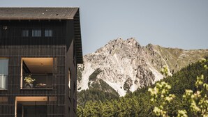 Un edificio moderno con balcón, telón de fondo montañoso y bosque denso.