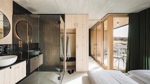 Un dormitorio moderno con una cama grande, un baño con cabina de ducha de vidrio y vistas a la ciudad a través de amplios ventanales.