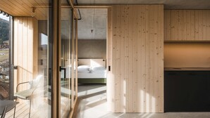 Un dormitorio moderno con puerta de cristal que da a un balcón, paredes de madera y una cama con ropa blanca.