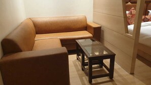 A small, modern room with a brown leather sofa, a glass coffee table, and a wooden bed frame. - HOTEL JR GRAND (Amritsar)