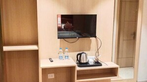 A hotel room with a wooden wardrobe, a small desk with a kettle, a TV, and two water bottles. - HOTEL JR GRAND (Amritsar)