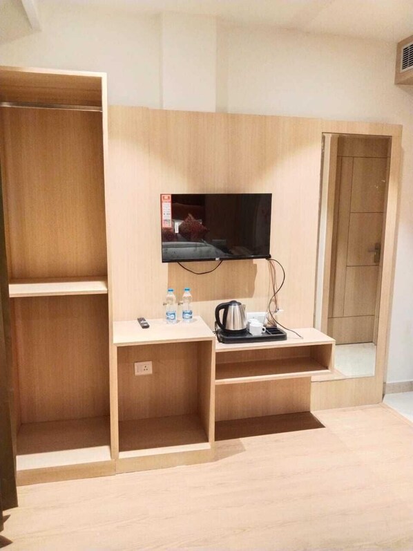 A hotel room with a wooden wardrobe, a small desk with a kettle, a TV, and two water bottles. - HOTEL JR GRAND (Amritsar)