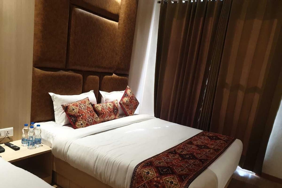 A hotel room with a large bed, a headboard, a bedside table with water bottles, and a window with curtains.