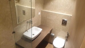 A bathroom with a glass-enclosed shower, a white sink, and a toilet. - HOTEL JR GRAND (Amritsar)