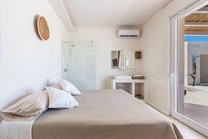 Quarto com cama, mesa de cabeceira, espelho e porta de vidro que se abre para uma varanda.