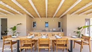 A dining area with a wooden table and chairs, a kitchen in the background, and a ceiling with wooden beams. - 4096 Villa Gabriella by Perle di Puglia (Sannicola)