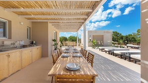 An outdoor dining area with a long wooden table set for six, surrounded by chairs, under a bamboo roof. - 4096 Villa Gabriella by Perle di Puglia (Sannicola)