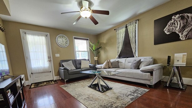 A living room with a sofa, a coffee table, a ceiling fan, a clock, and a tiger painting on the wall.
