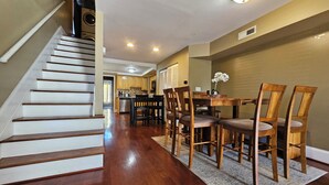 A staircase leading to a kitchen area with wooden flooring, a dining table with chairs, and a ceiling light.