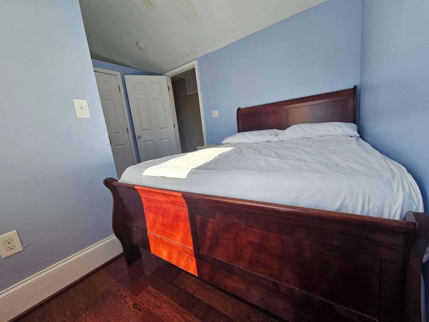 Une chambre avec un lit en bois, une porte et un interrupteur sur le mur.