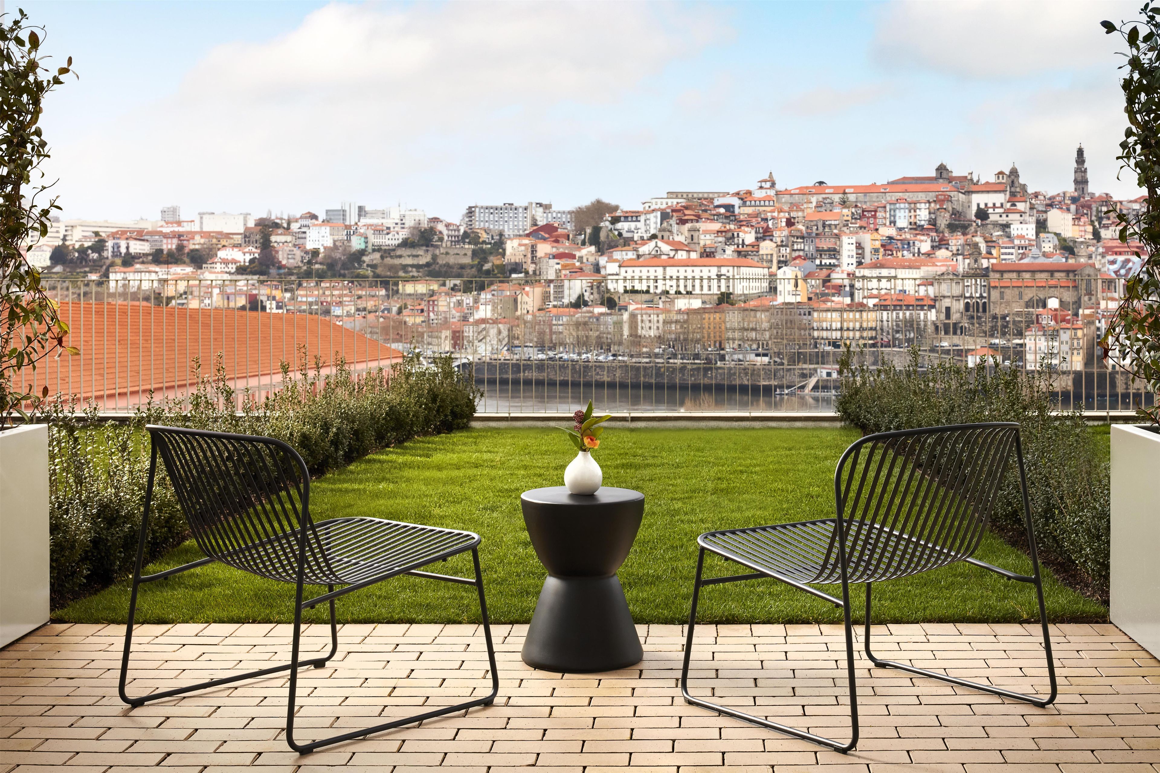 Eine Terrasse mit zwei Metallstühlen und einem Tisch, mit Blick auf eine Stadtlandschaft mit roten Dächern.