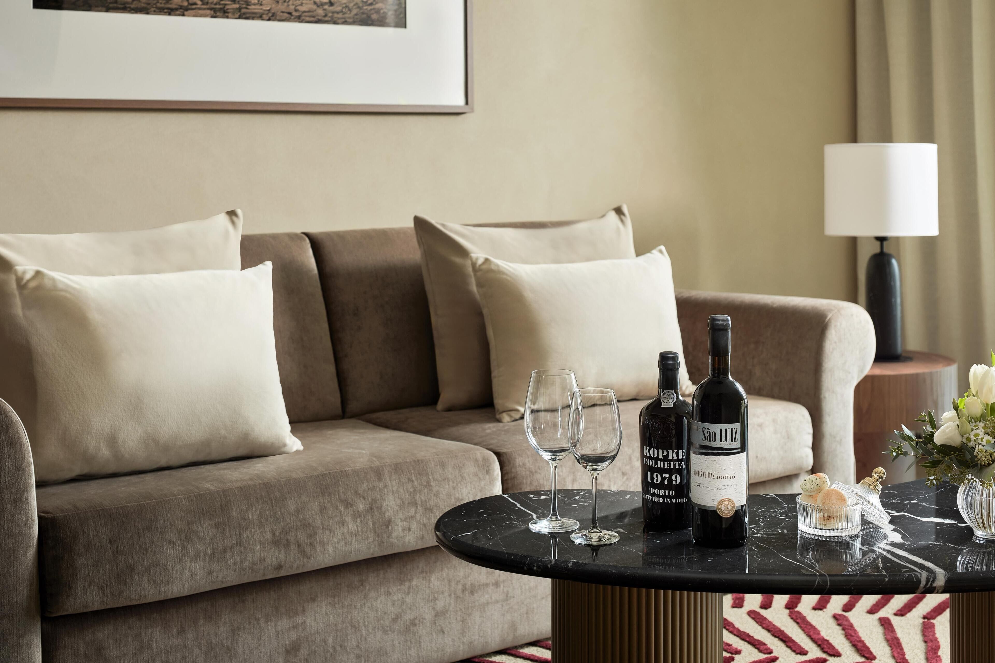 Un salon moderne avec un canapé, une table basse ronde, deux verres à vin et deux bouteilles de vin.