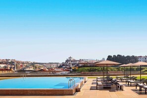 Piscina en la azotea con sillones de descanso y sombrillas, con vistas a un paisaje urbano que incluye un puente y edificios.