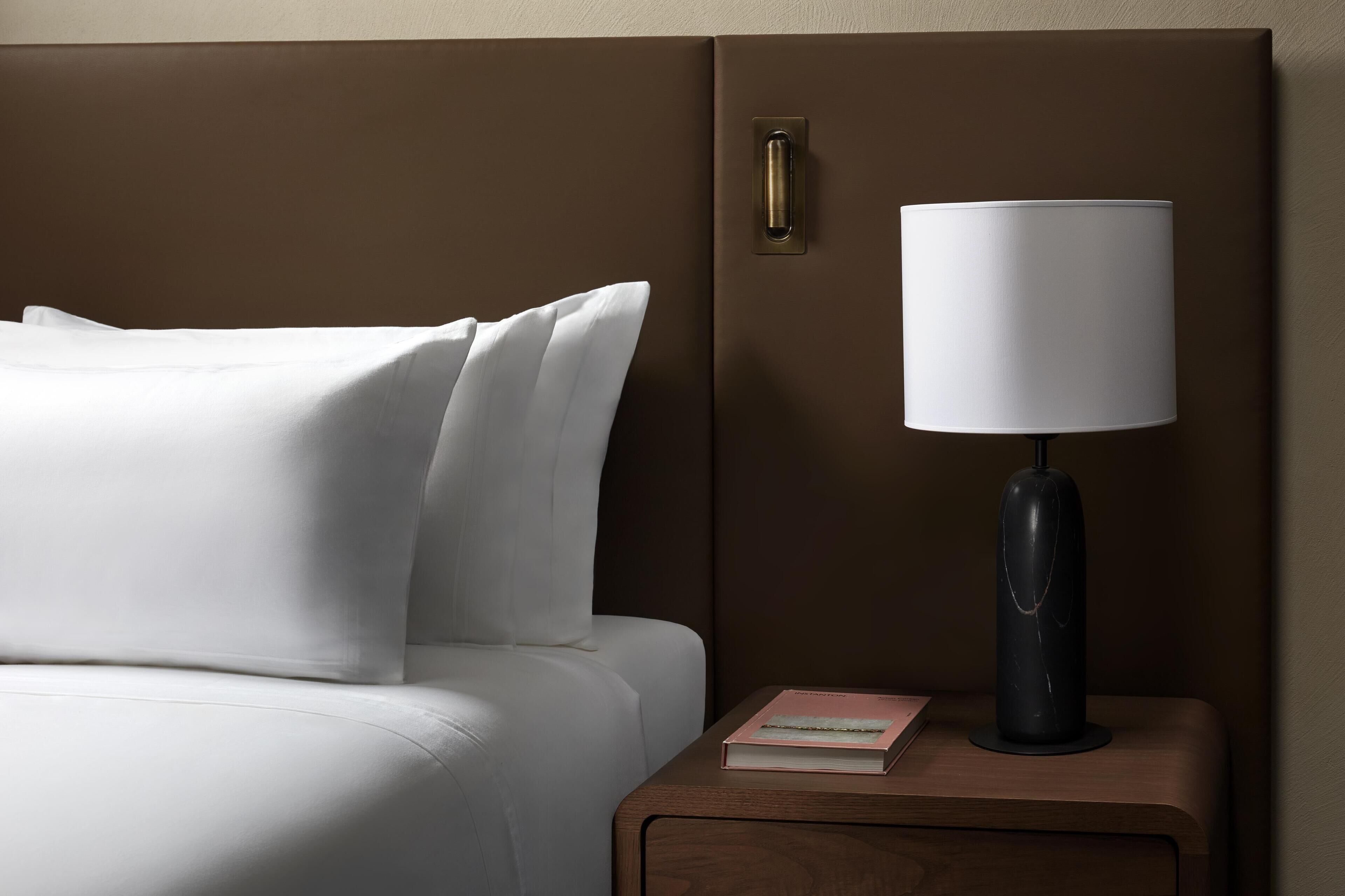 Una habitación de hotel con una cama, una mesita de noche con una lámpara y un libro.