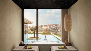 A spa room with two beds, a large window with a city view, a bathtub, and a hanging light fixture. - Tivoli Kopke Porto Gaia Hotel (Vila Nova de Gaia)