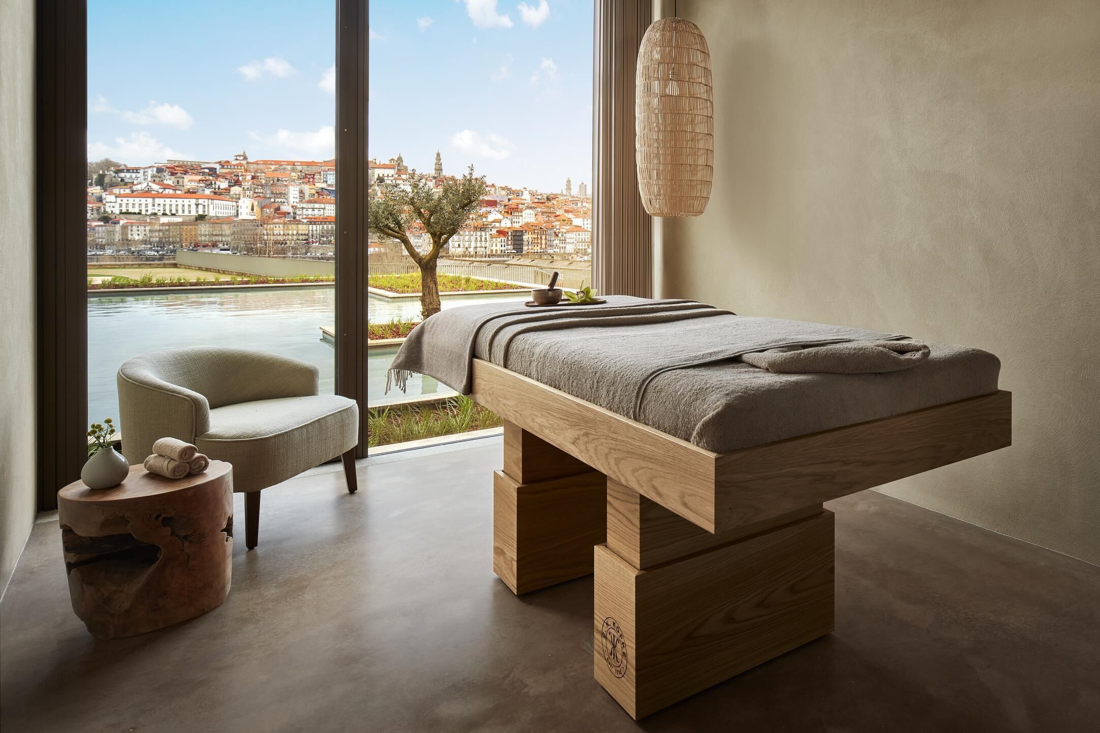 A modern bedroom with a large window, a wooden bed, a side table, and a chair.