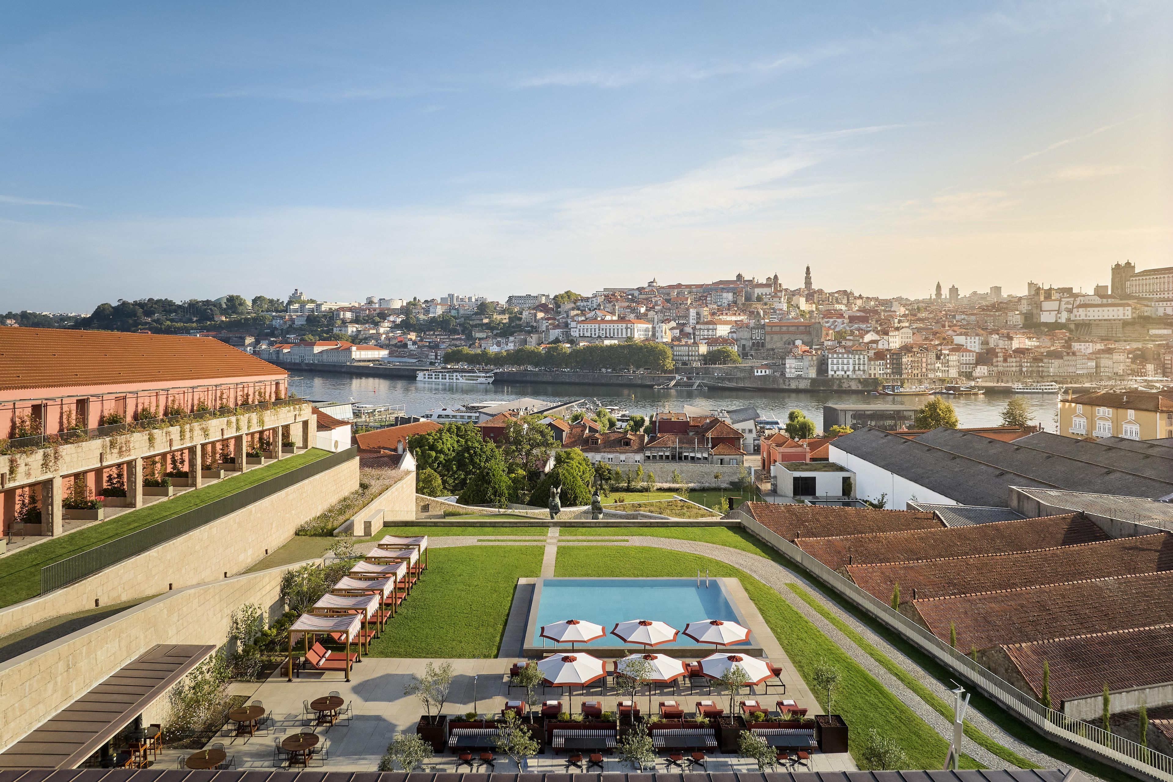 A hotel courtyard with outdoor seating and a pool, overlooking a river and cityscape.