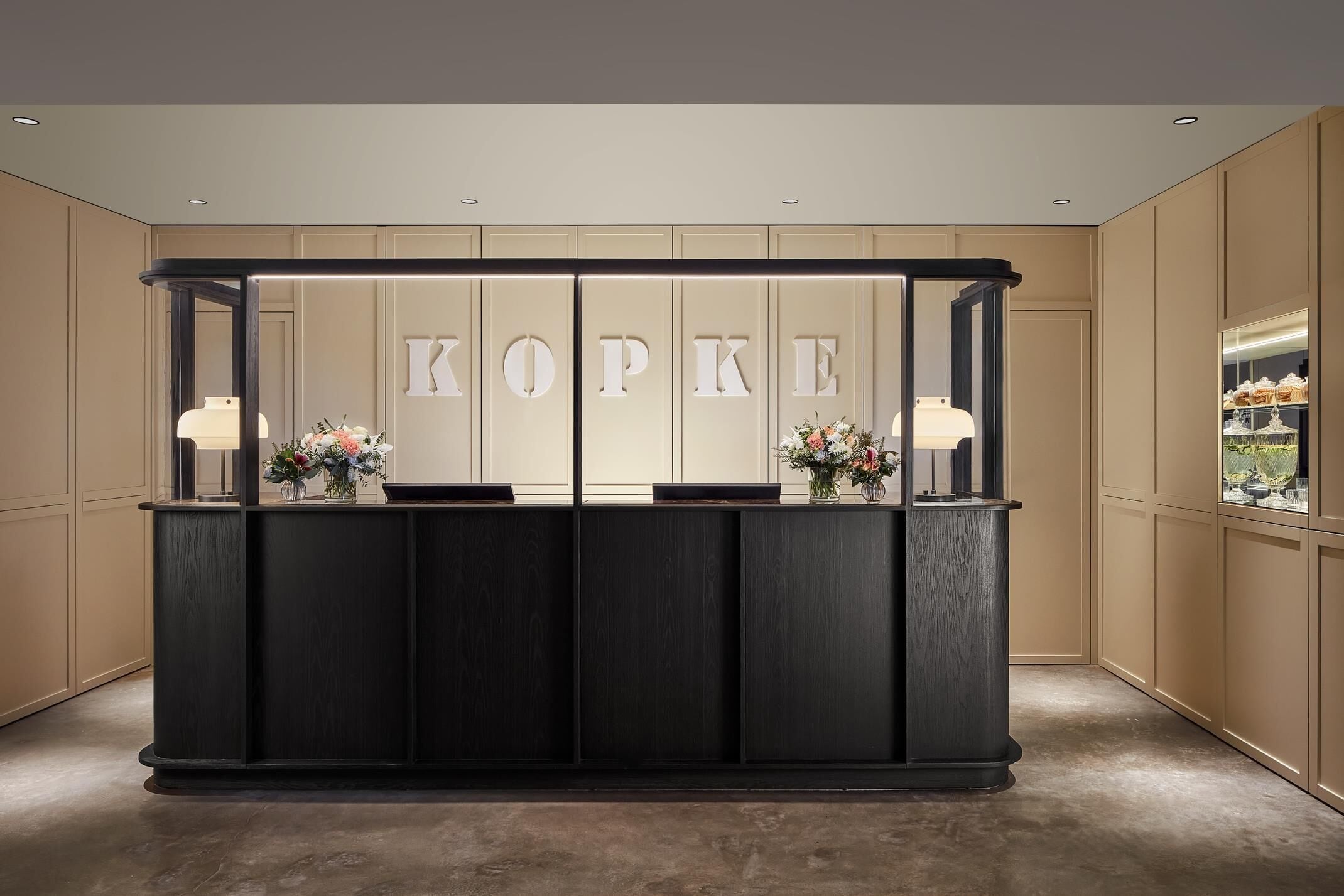 A reception desk with a dark wood finish, two lamps, and a floral arrangement.