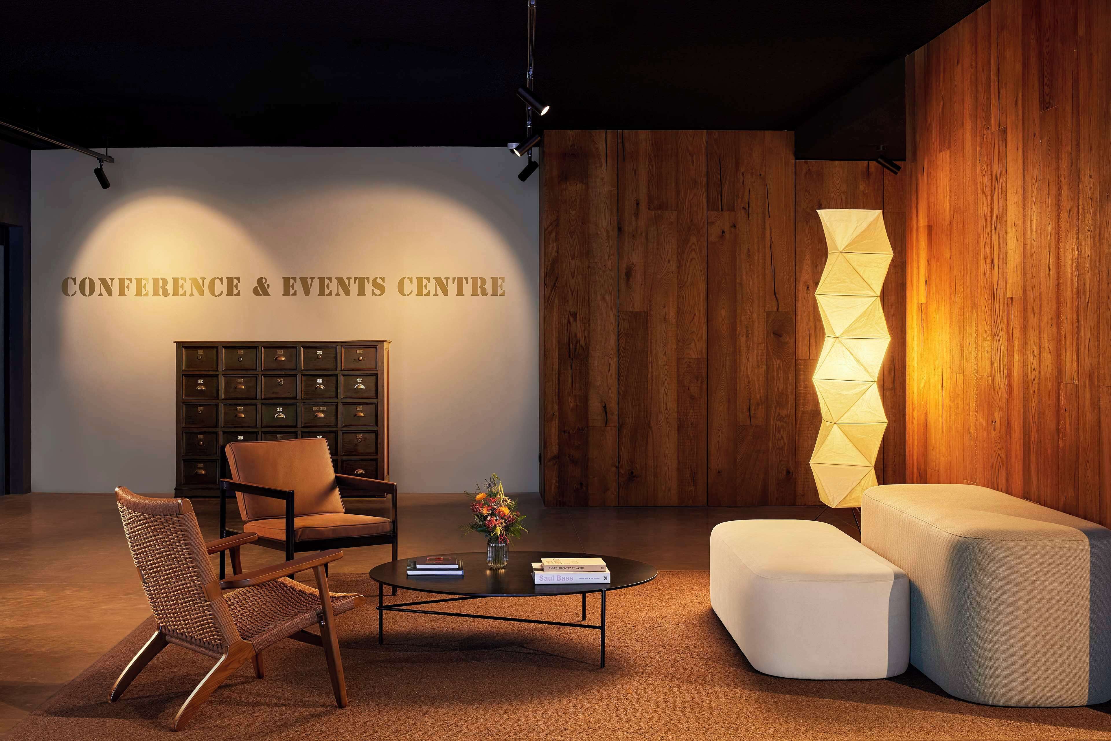 A conference room with a wooden wall, a sofa, a chair, a coffee table, and a bookshelf.