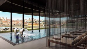 A modern indoor swimming pool with a city view, a water feature, and a seating area. - Tivoli Kopke Porto Gaia Hotel (Vila Nova de Gaia)