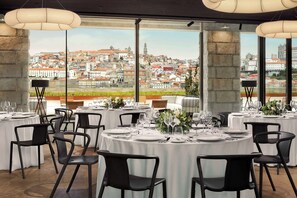 A restaurant with round tables set for dining, large windows offering a city view, and modern pendant lighting. - Tivoli Kopke Porto Gaia Hotel (Vila Nova de Gaia)