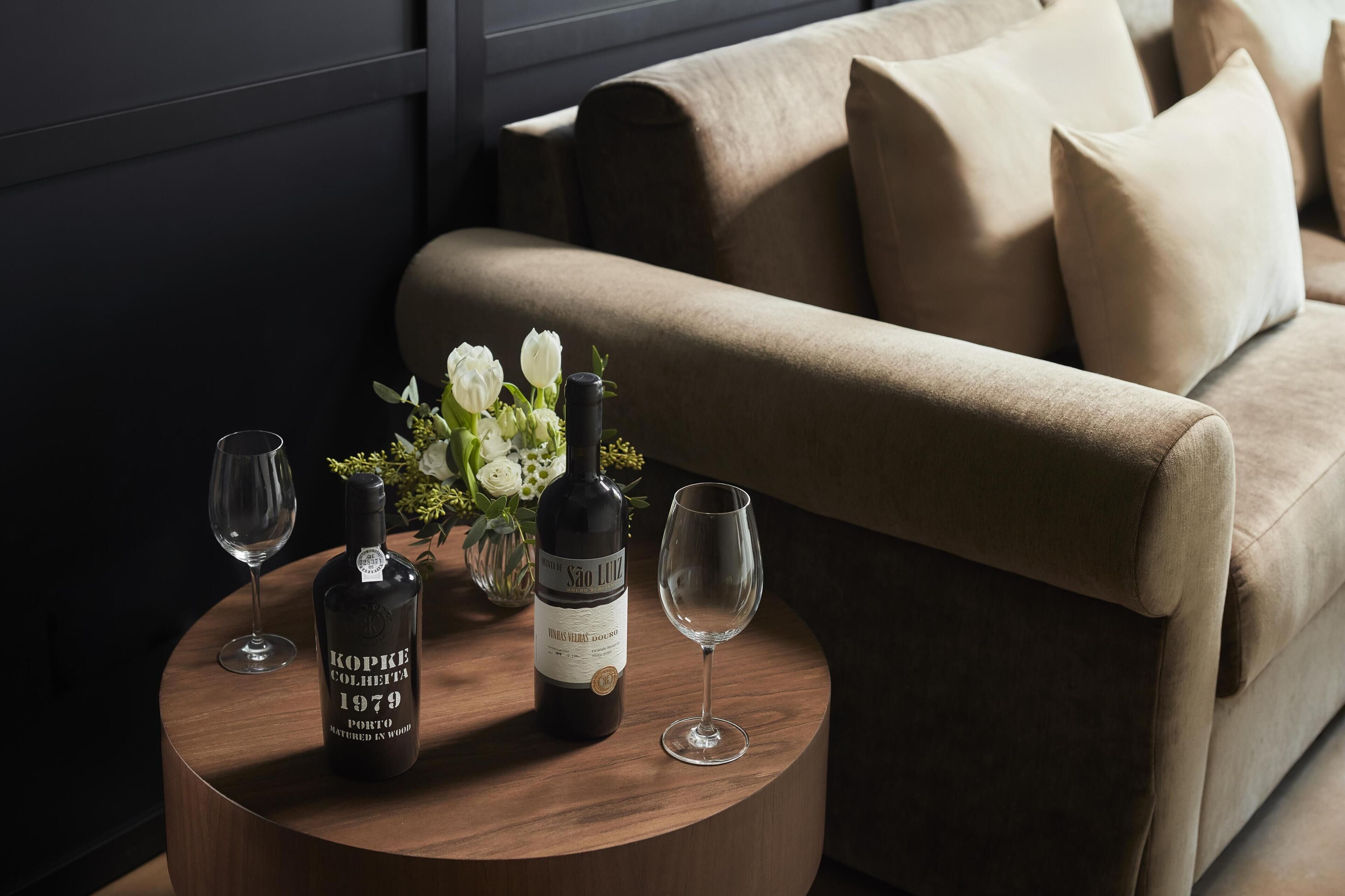 Una mesa redonda de madera con una botella de vino, una copa y un jarrón con flores.