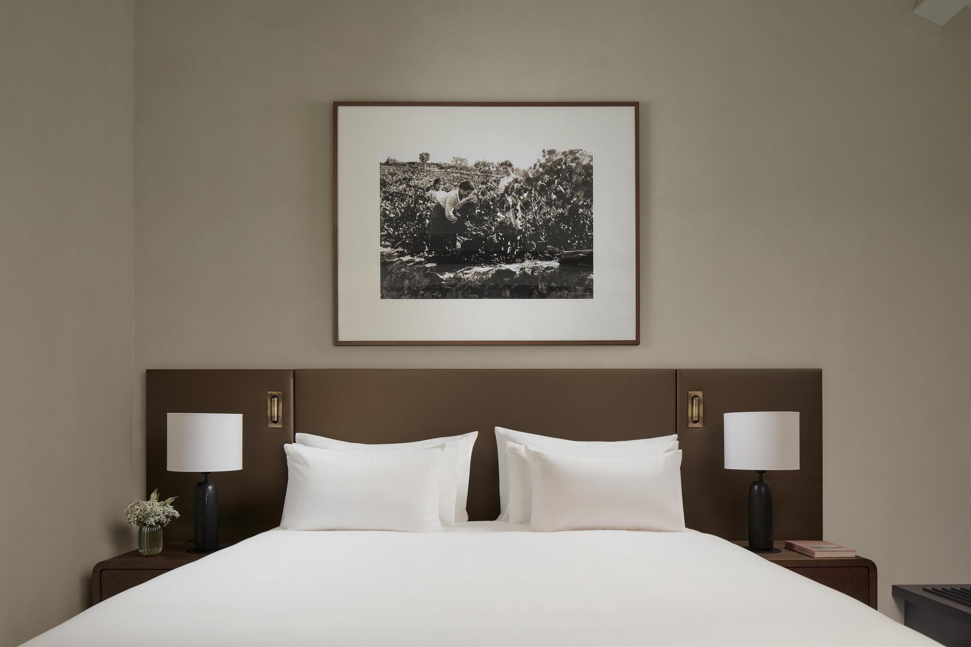 A hotel room with a large bed, two bedside tables with lamps, a framed picture on the wall, and a nightstand with a vase of flowers.