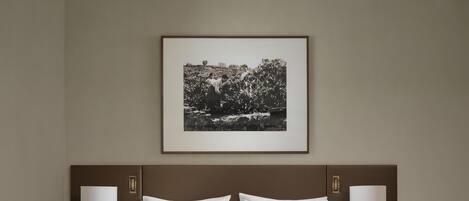 A hotel room with a large bed, two bedside tables with lamps, a framed picture on the wall, and a nightstand with a vase of flowers.