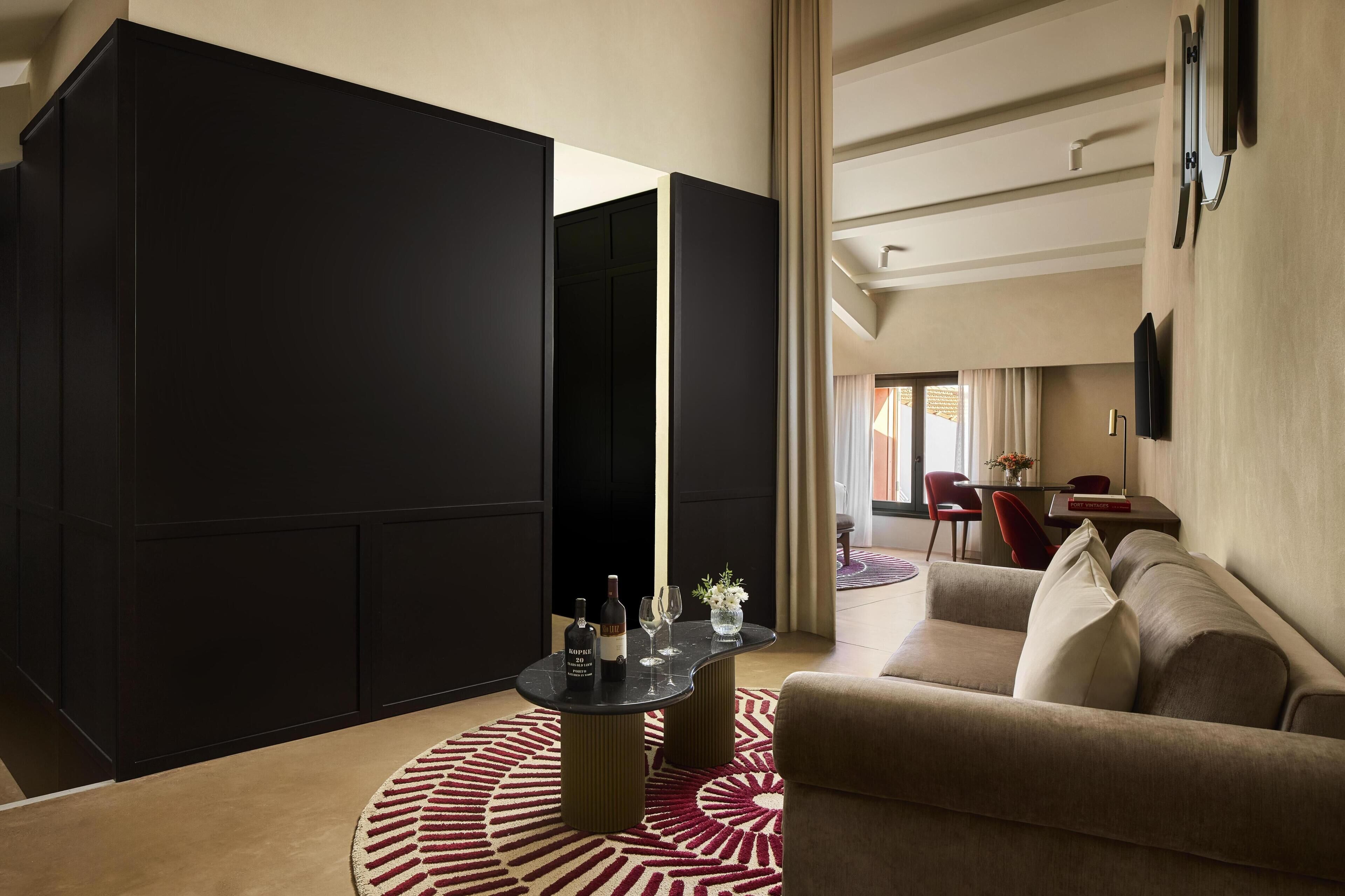 A modern living room with a black partition, a round coffee table with wine glasses and bottles, a beige sofa, and a red patterned rug.