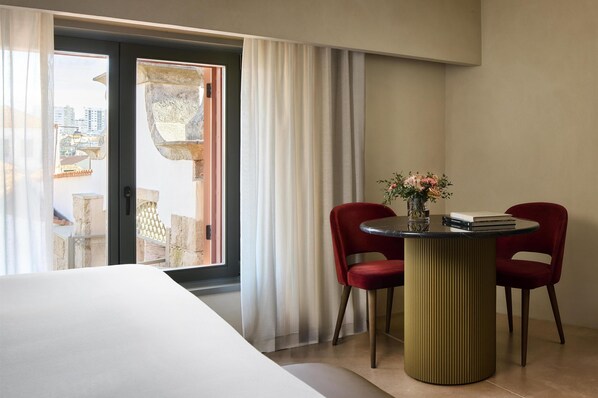 A hotel room with a bed, a table with two chairs, a vase with flowers, and a view through a sliding door.